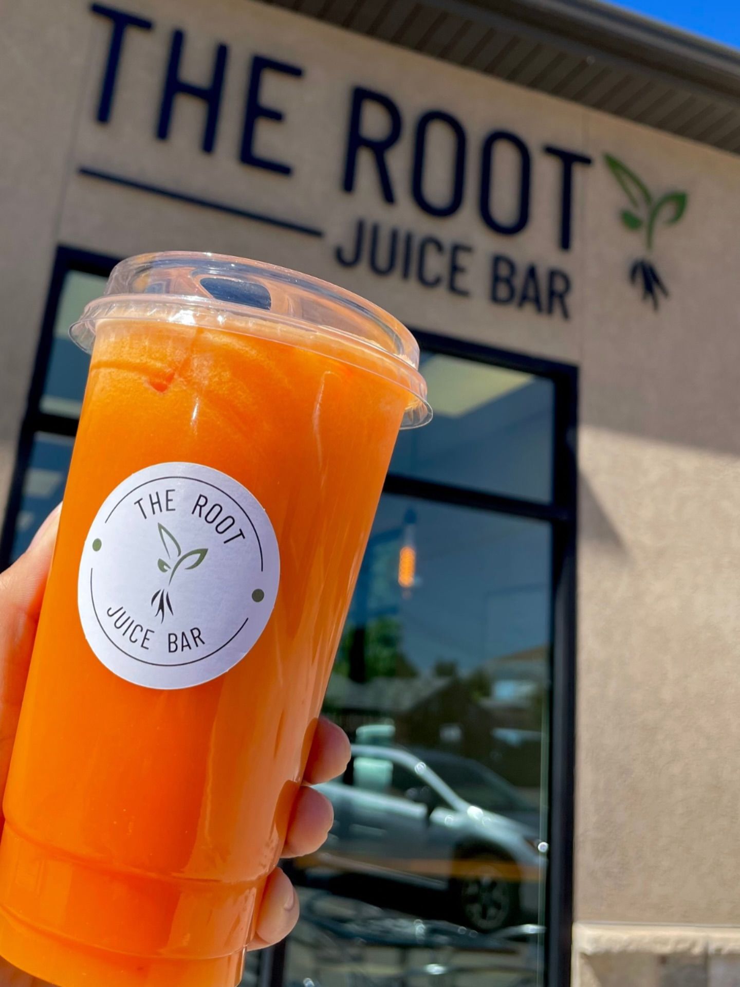 A hand holds a plastic cup of bright orange juice in front of 