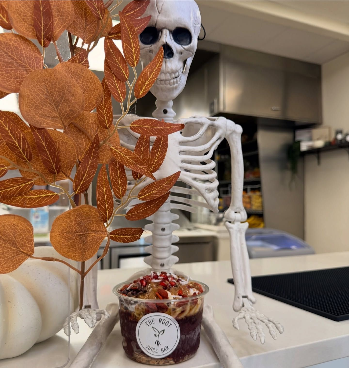 A plastic cup of an acai bowl sits in front of a decorative skeleton and orange faux leaves on a counter.
