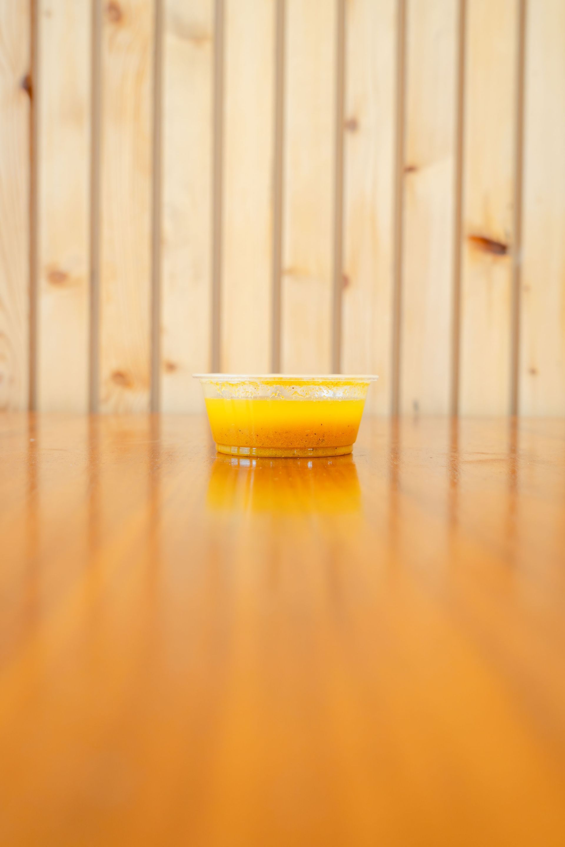 A hand holds two plastic syringes filled with orange liquid against a green, leafy background.