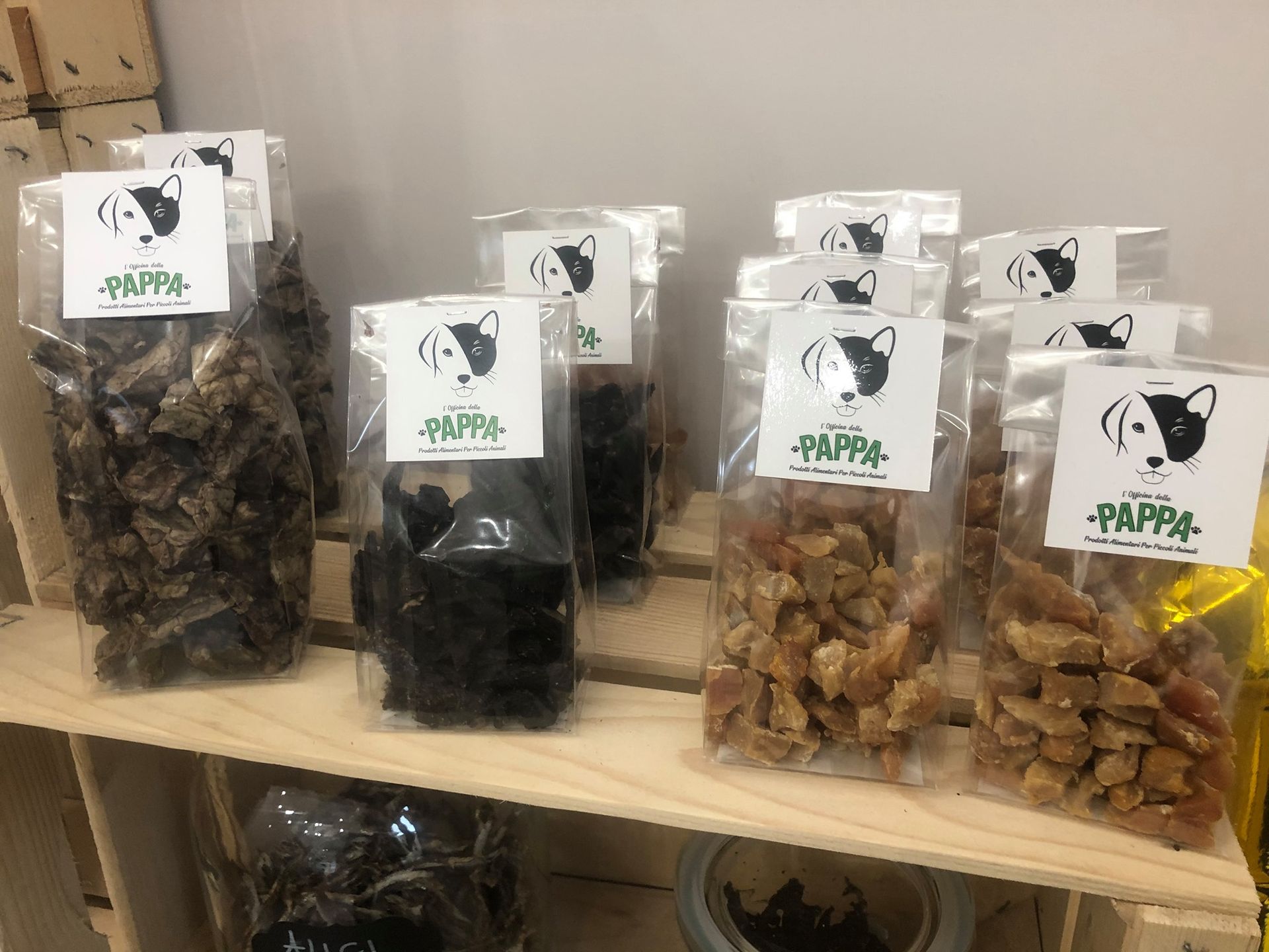 Snack per cani in sacchetti trasparenti su uno scaffale di legno, ogni sacchetto è etichettato con il logo di un cane e la scritta 