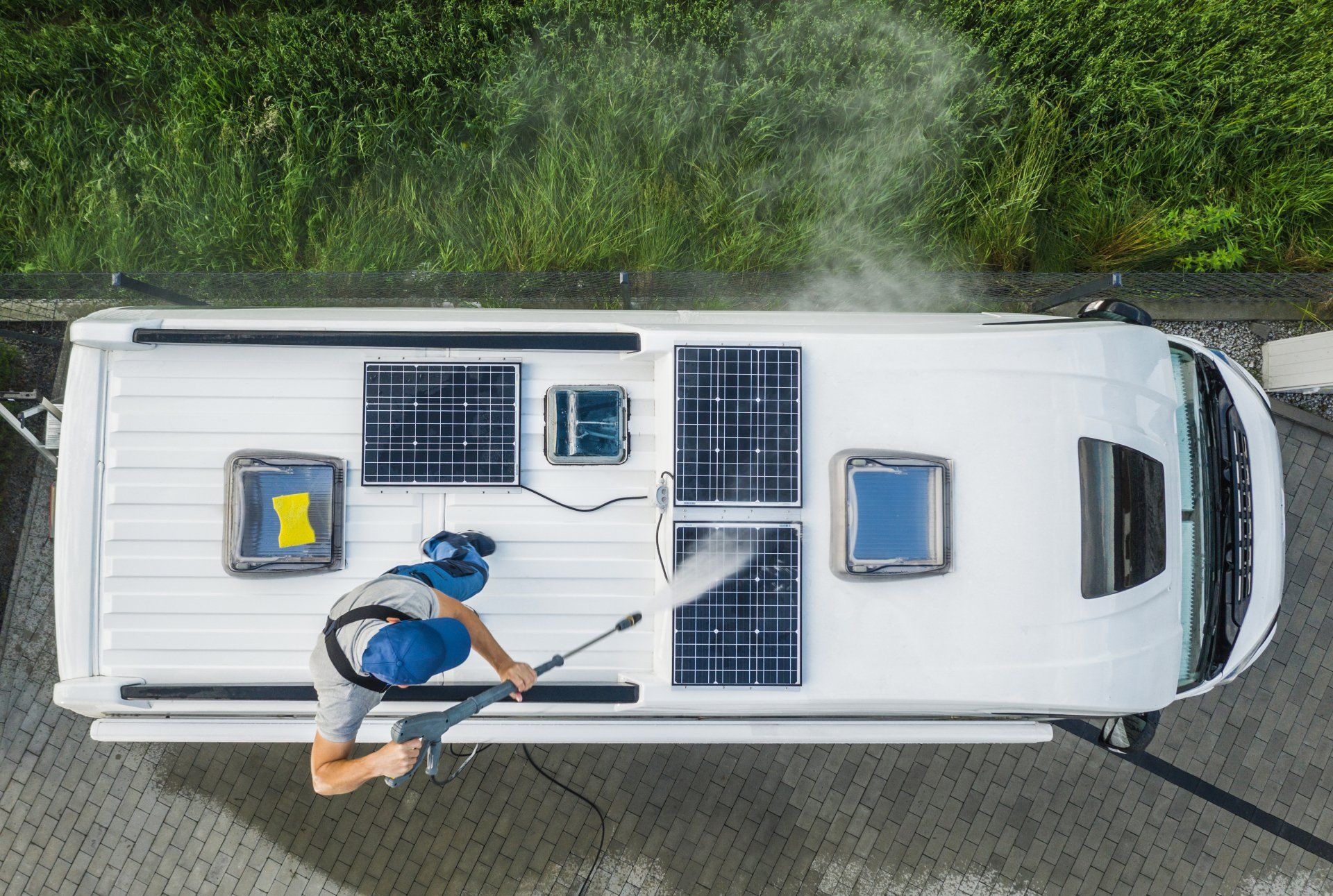 A worker power washing solar panels on top of an RV