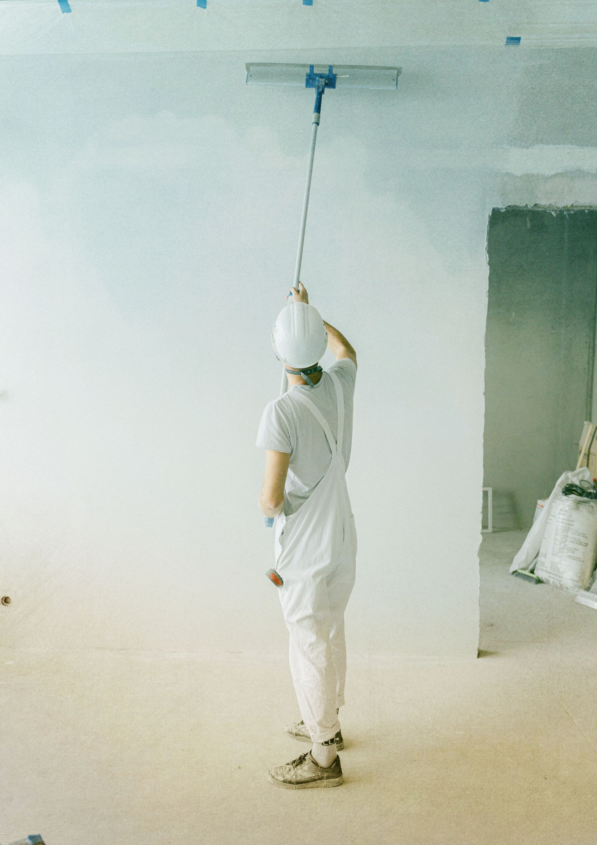 A man wearing a hard hat and gloves is using a drill on a wall.
