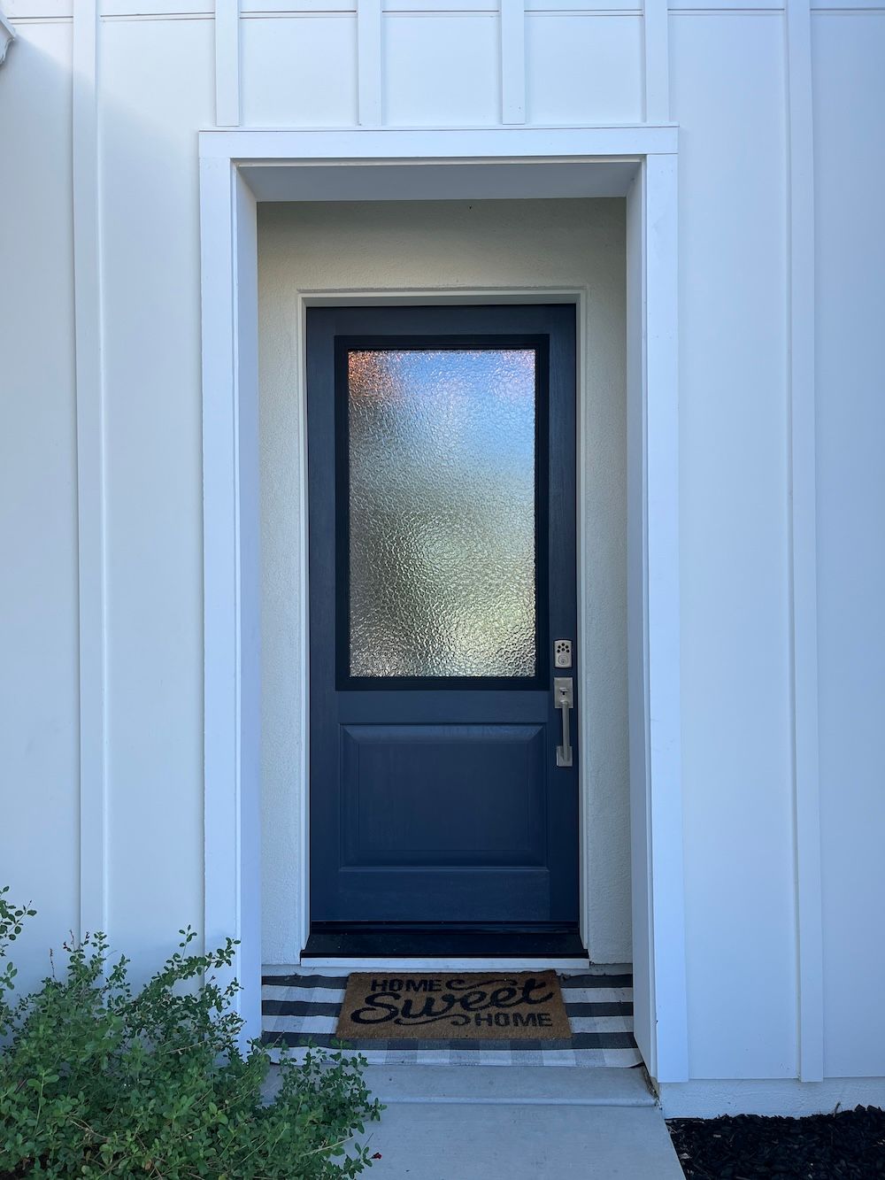 A blue front door with a glass window is on a white house.