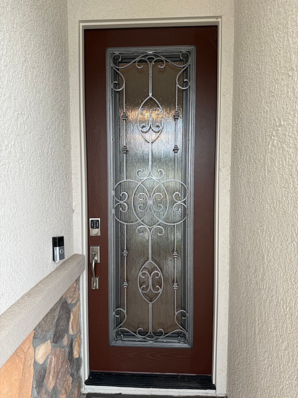 A brown door with a wrought iron design on it is on a white wall.
