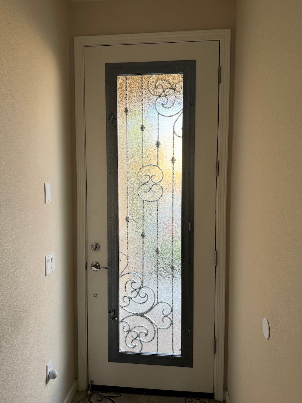 A white door with a wrought iron frame and stained glass is in a hallway.