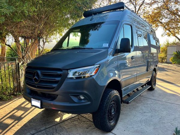 a black van is parked in a driveway next to a tree