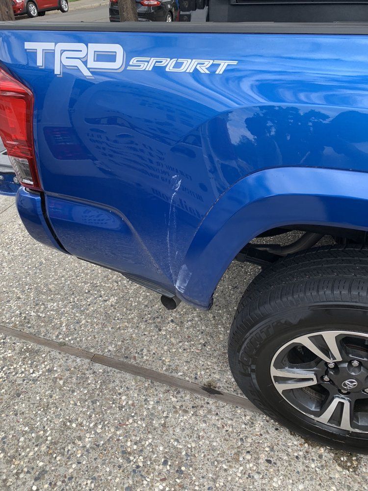 a blue toyota tacoma with a damaged fender is parked in a driveway