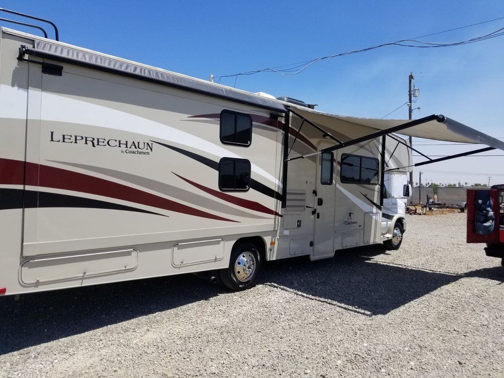 a rv with an awning is parked in a gravel lot