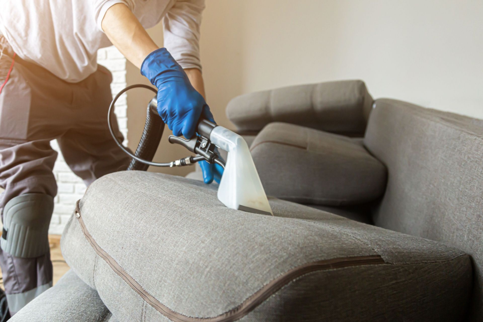 A man is cleaning a couch with a vacuum cleaner.