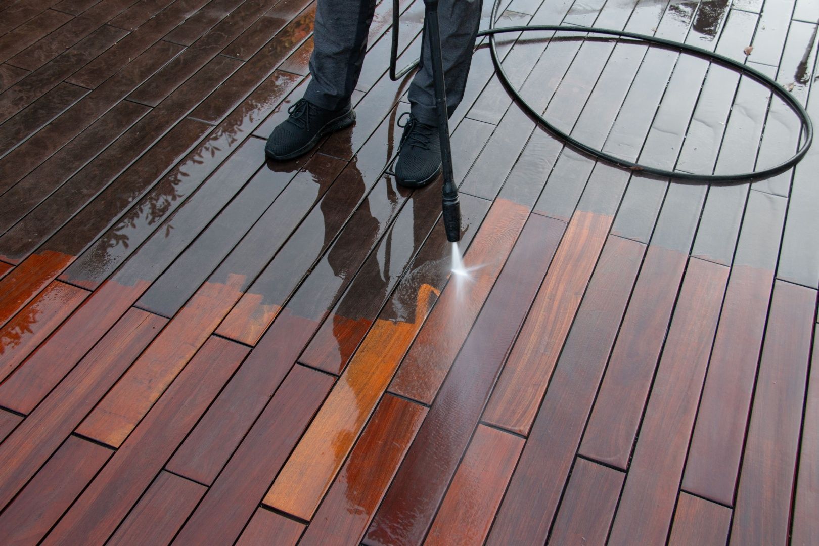 A person is cleaning a wooden deck with a high pressure washer.