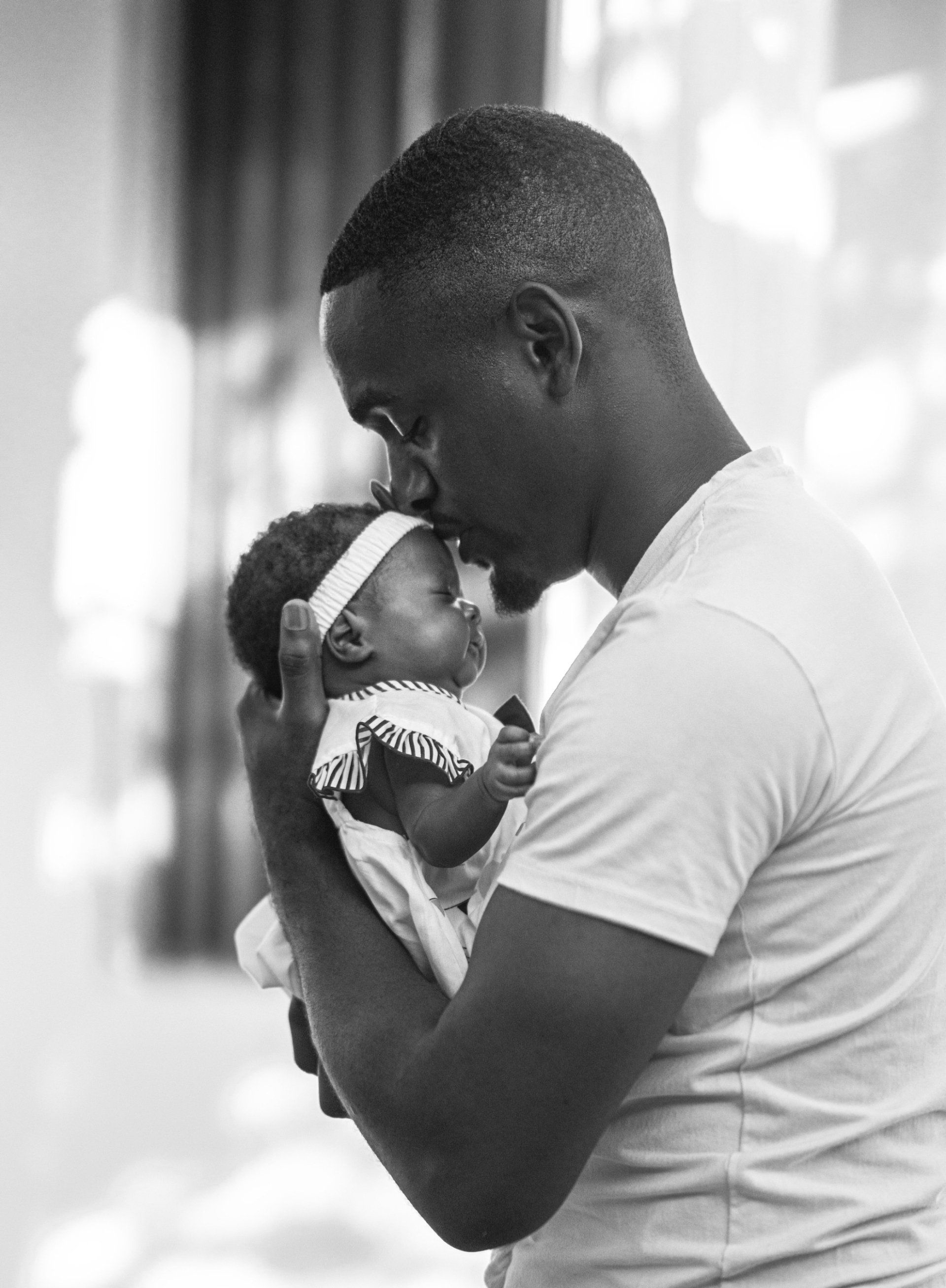 black and white photo of father kissing newborn daughter