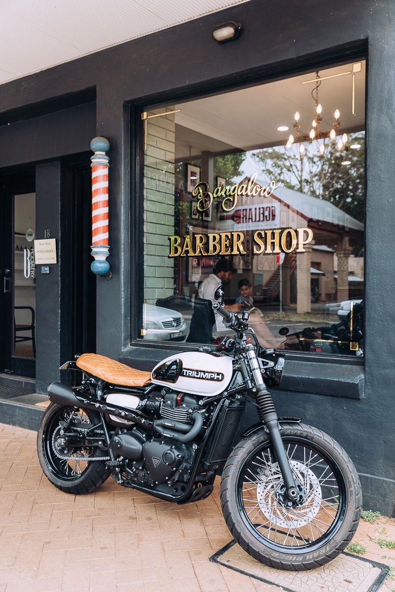 A motorcycle is parked in front of a barber shop.