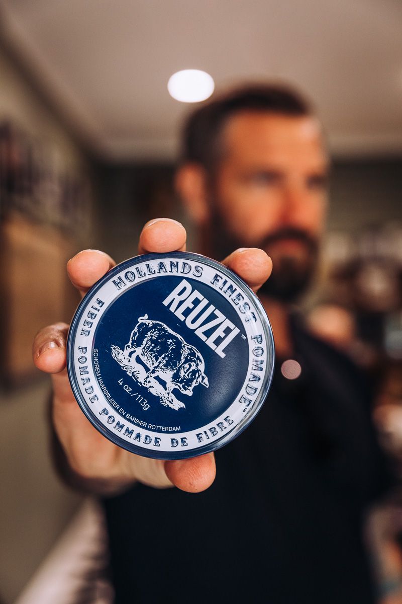 A man is holding a blue reuzel pomade in his hand.