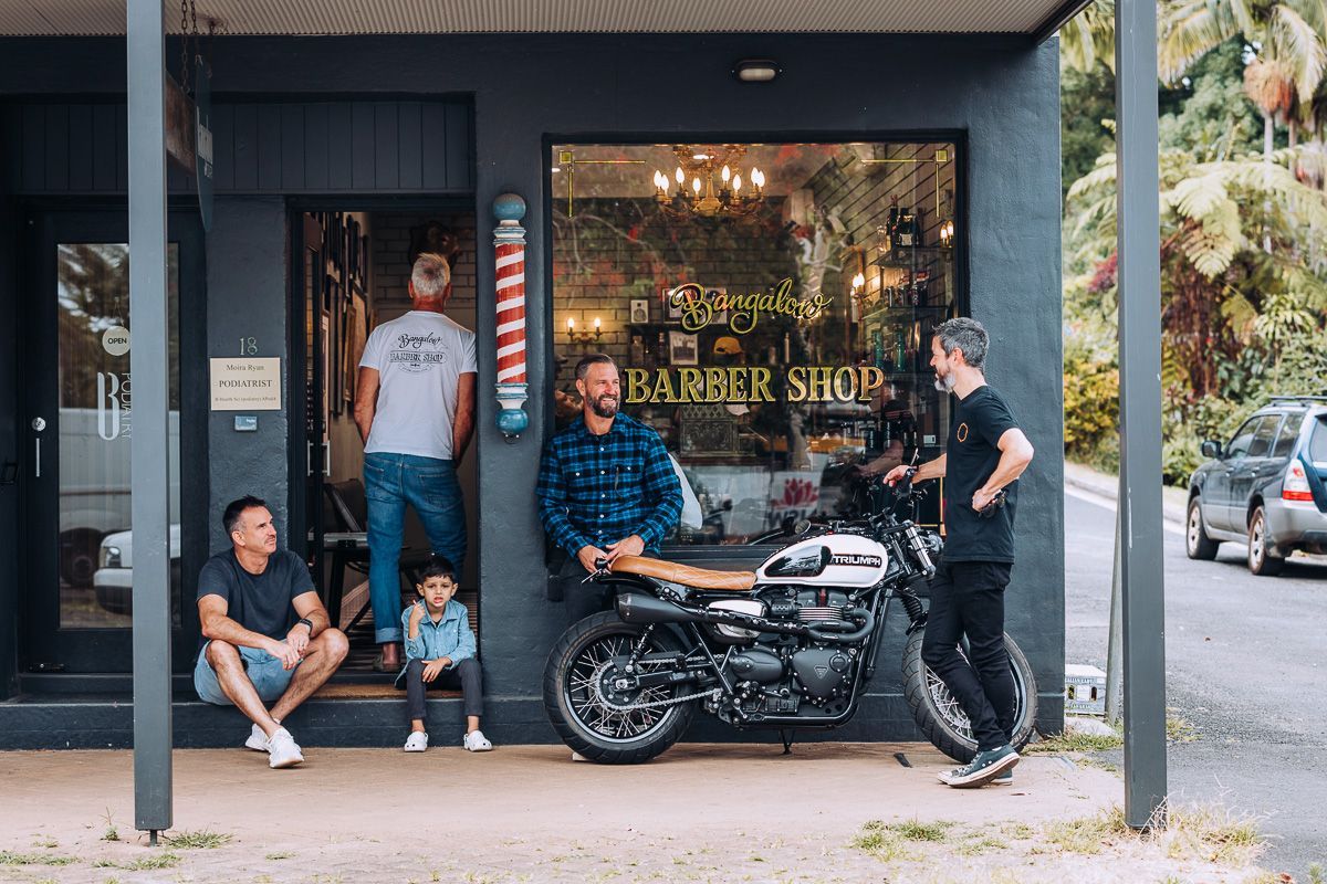 A group of men are standing outside of a barber shop.