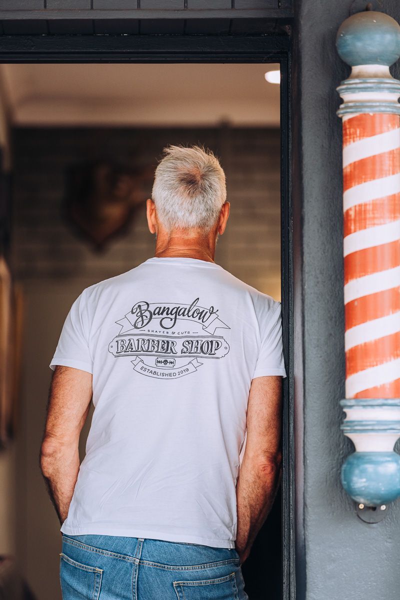 A man in a white t-shirt is standing in front of a barber pole.