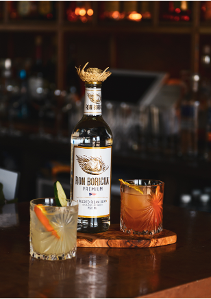 A bottle of Ron Boricua and two glasses of old fashioned rum are on a bar.