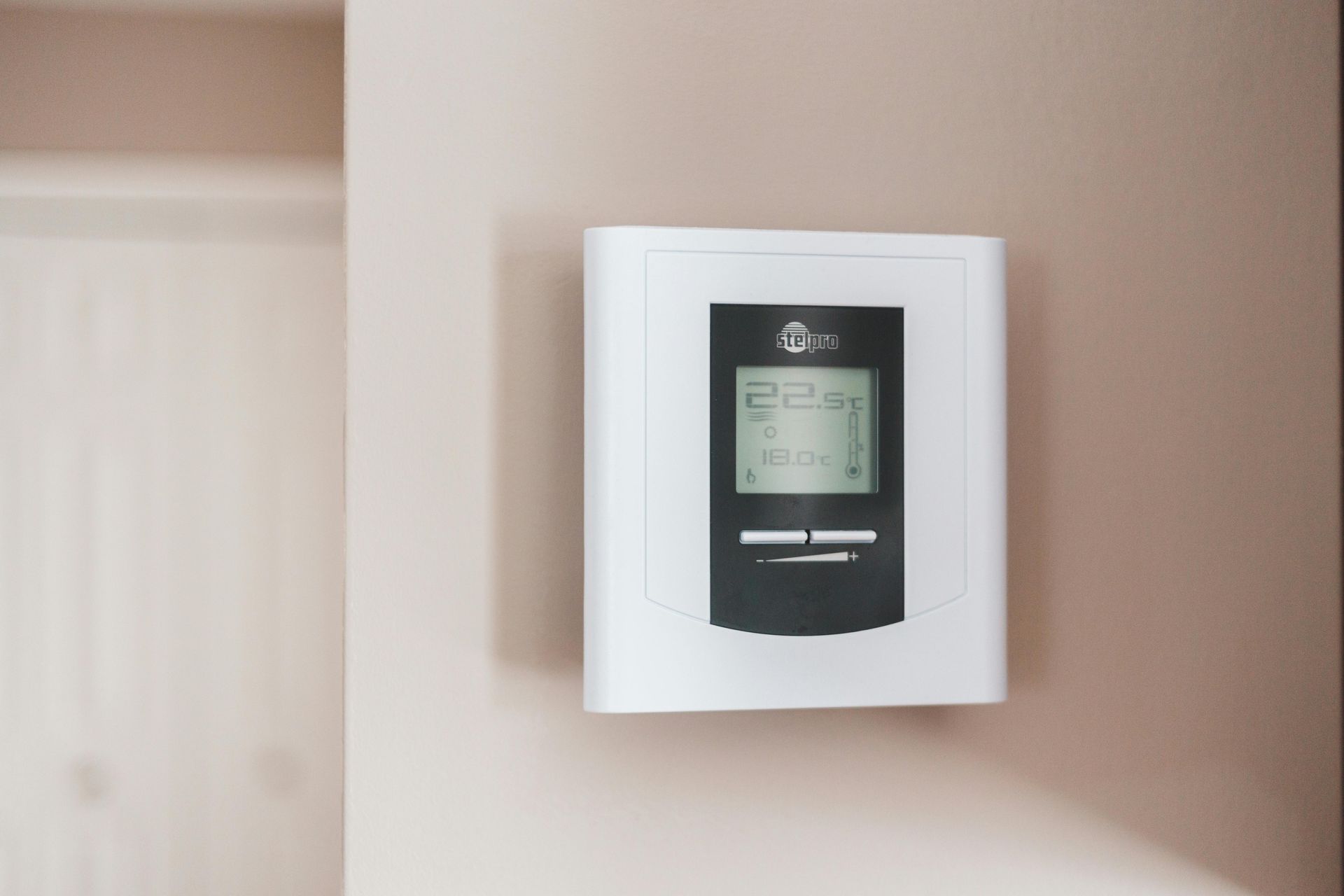 A white and black thermostat is hanging on a wall.