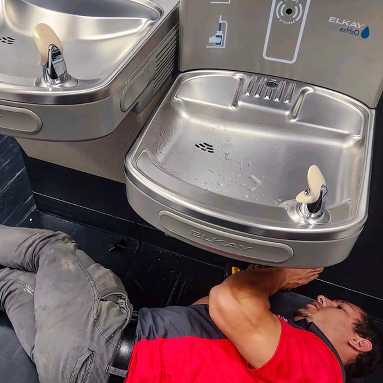 A man in a red shirt is laying under a water fountain