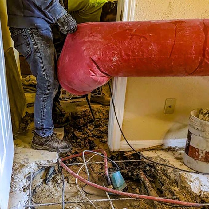 A man is holding a large red pipe in a room.