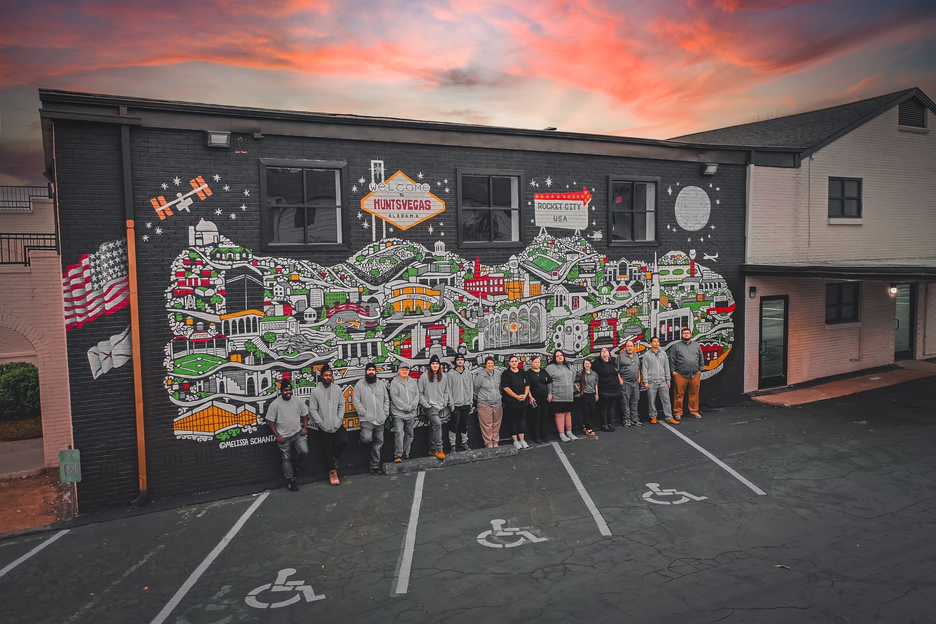 A group of people are standing in front of a large mural on the side of a building.