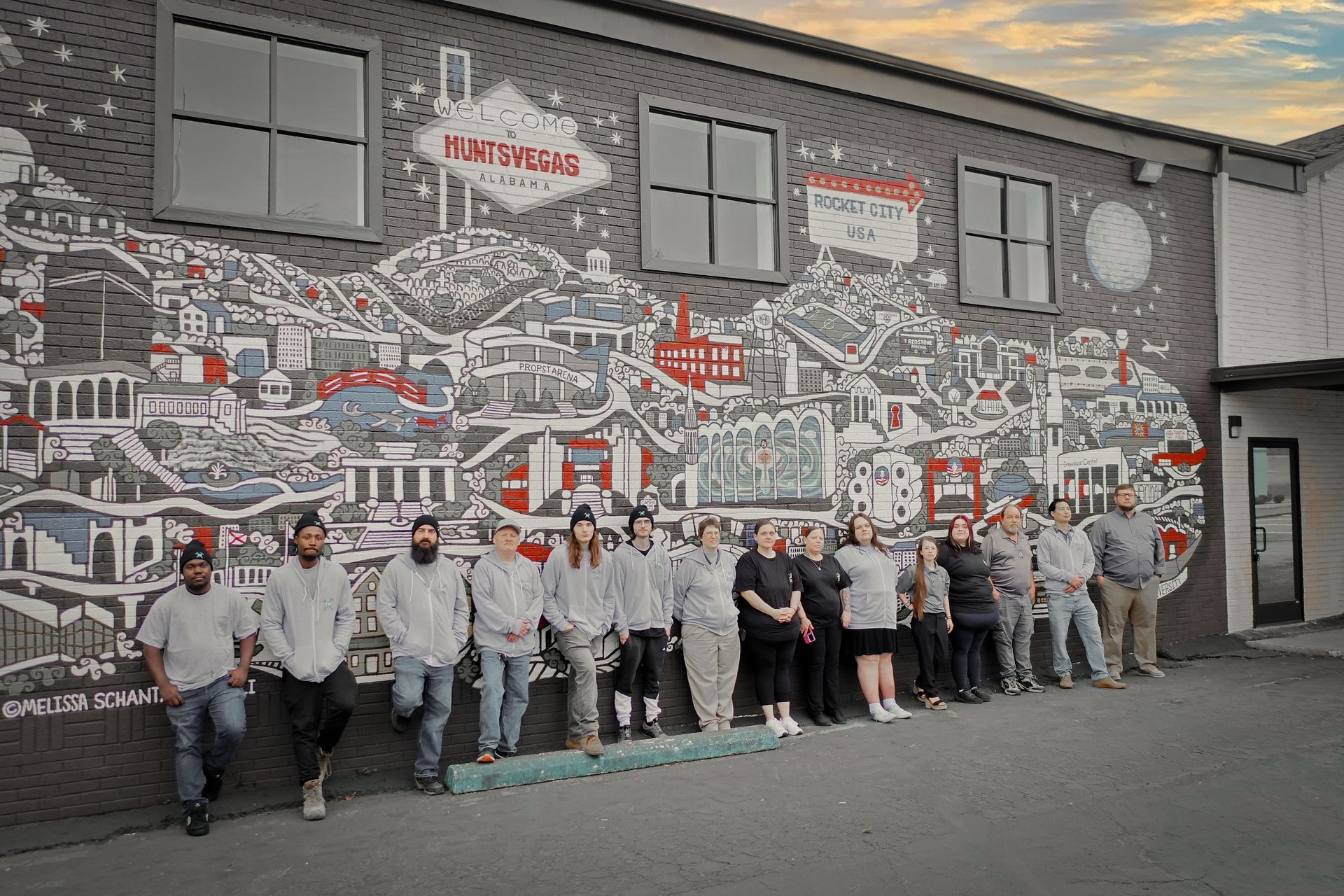 A group of people are standing in front of a large mural on the side of a building.