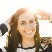 A woman in a striped sweater is smiling with the sun shining through her hair