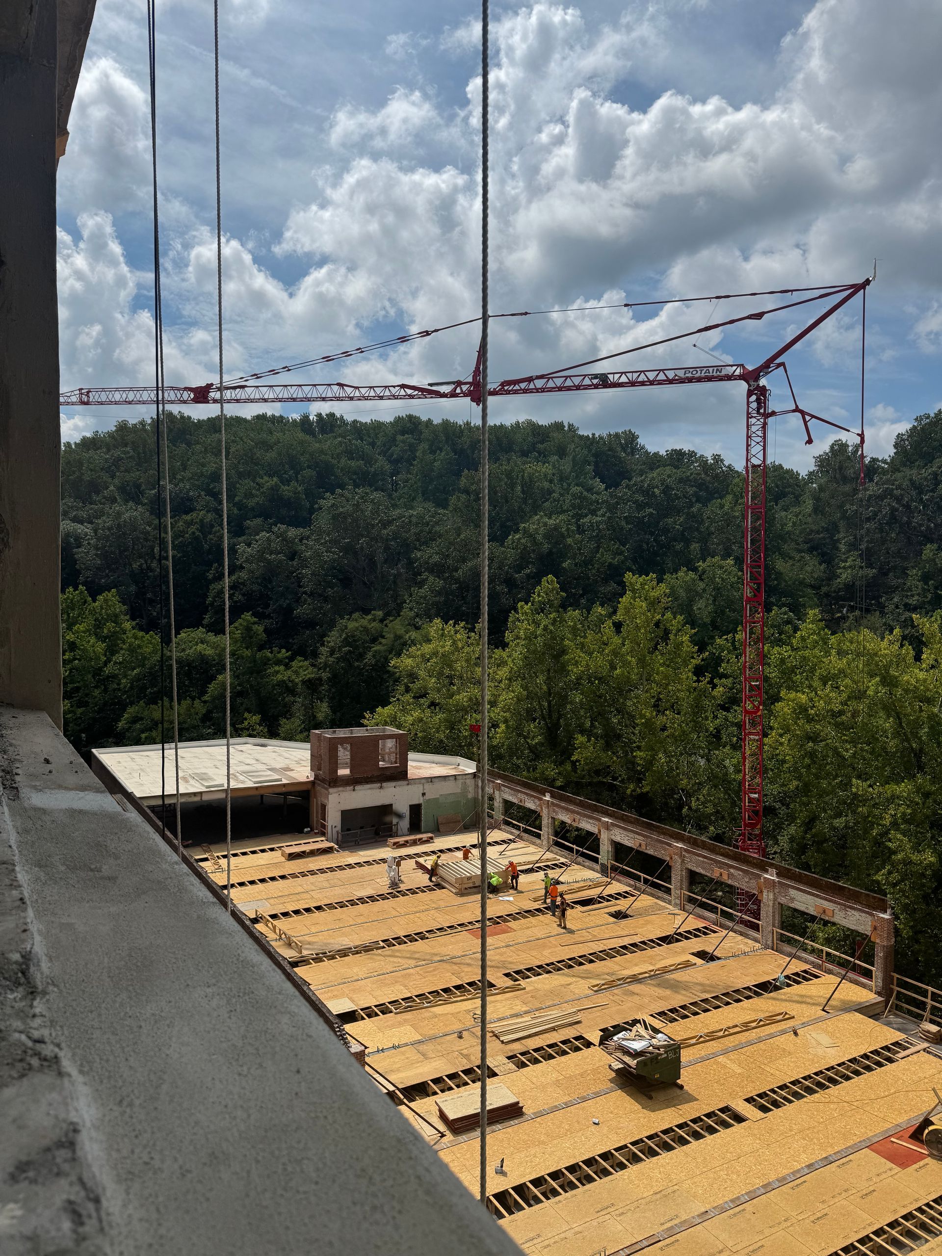 Construction site with rebar slab, crane boom, and forested hills under cloudy sky