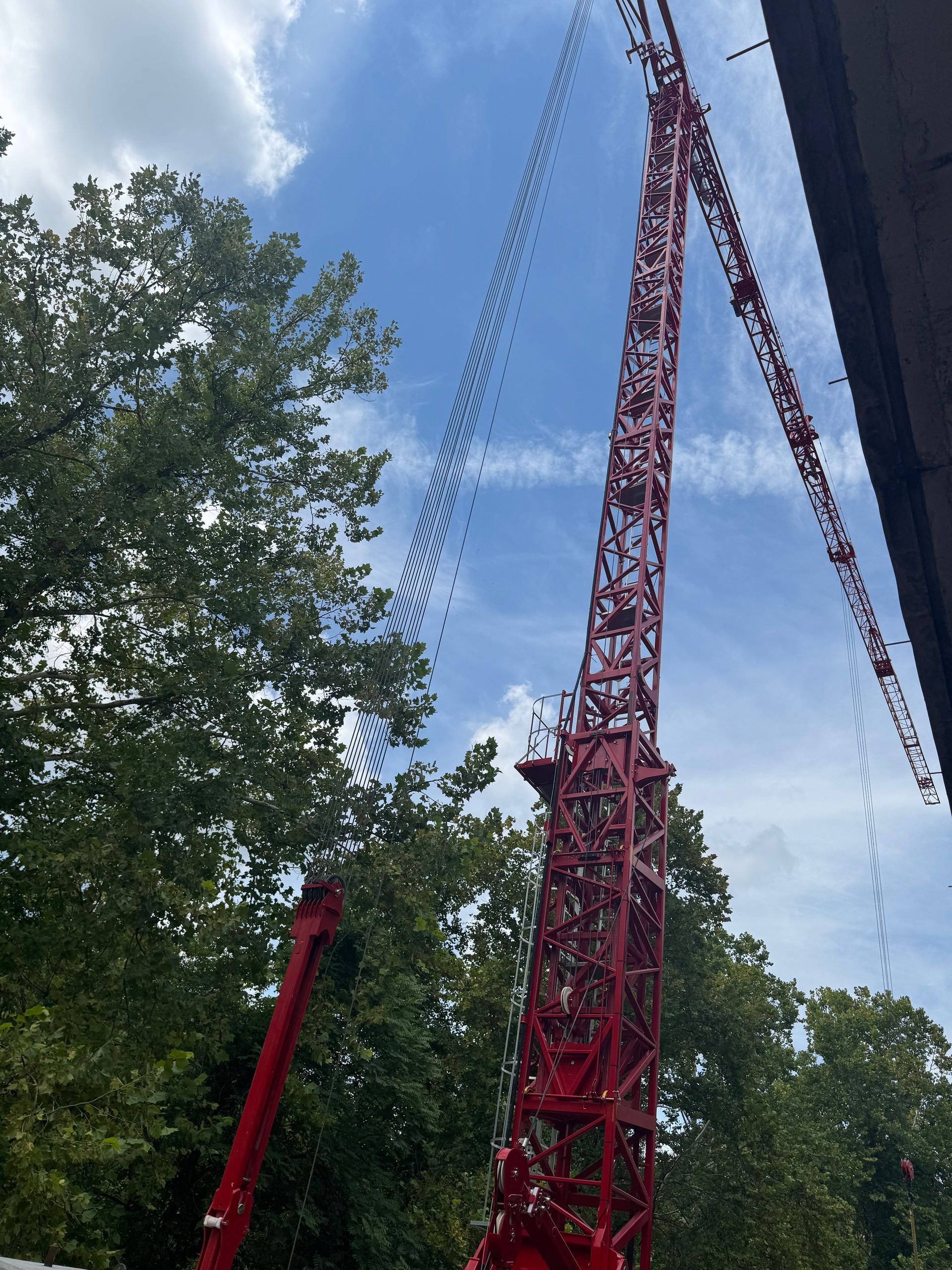 Tall red amusement ride tower against a blue sky with trees on the left