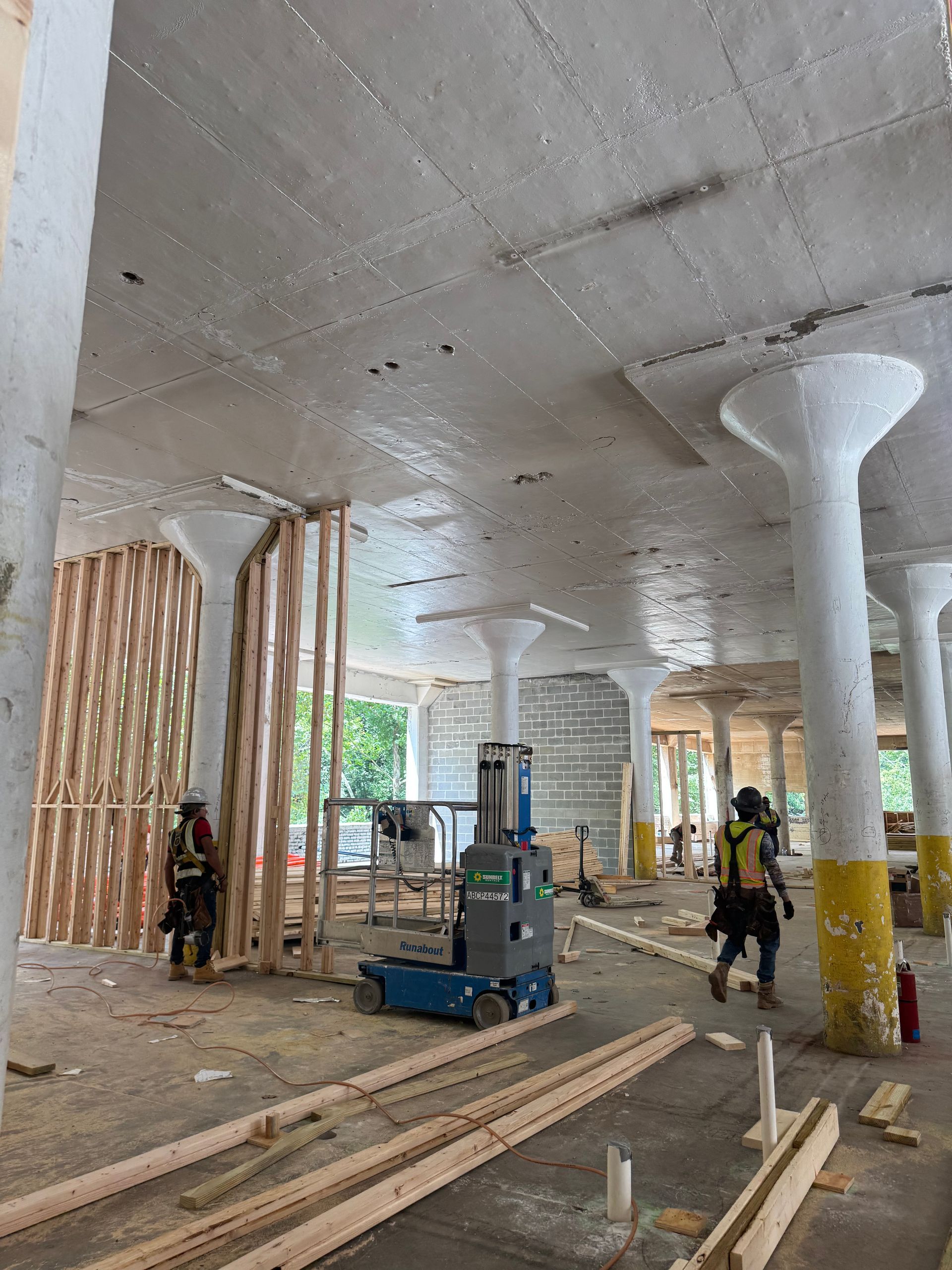 Construction site interior with workers, scaffolding, and concrete columns under a broad ceiling