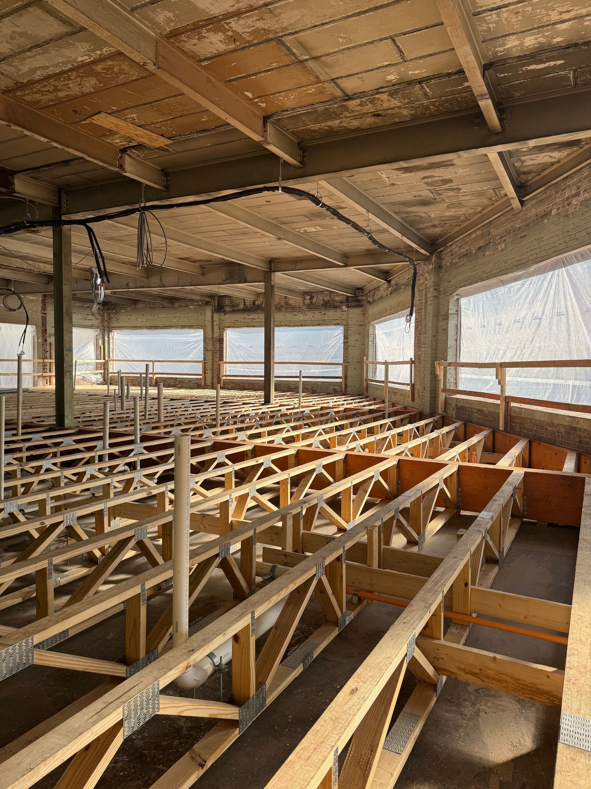 Open-frame interior under construction with exposed wooden beams and bright windows overlooking water.