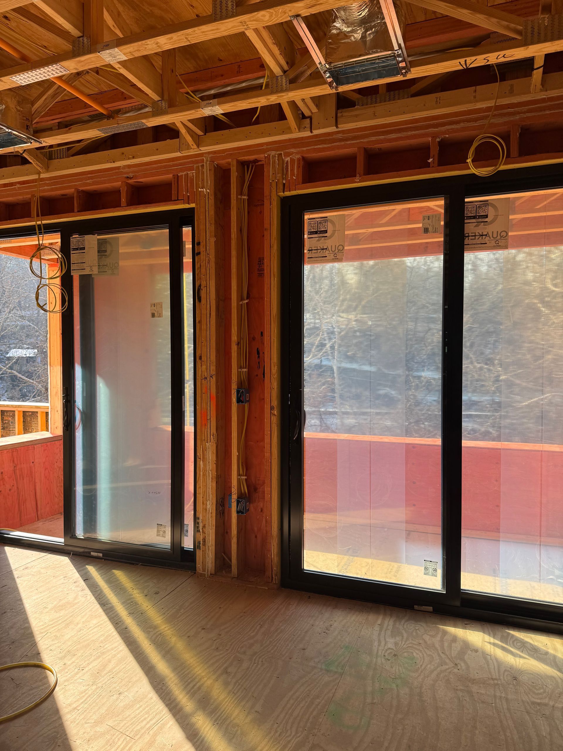 Unfinished room with exposed framing, large glass doors, and sunlight casting long shadows on the floor.