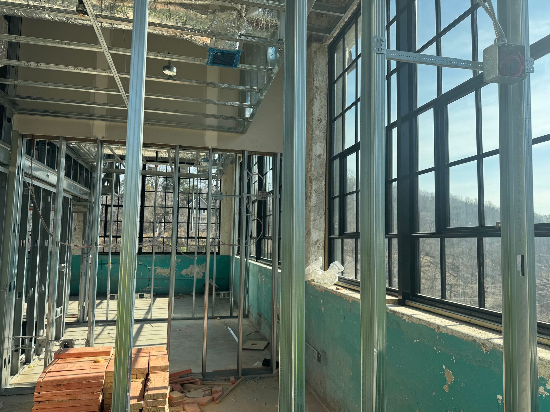 Interior of a sunlit building under construction, with metal framing, green walls, and floor-to-ceiling windows.