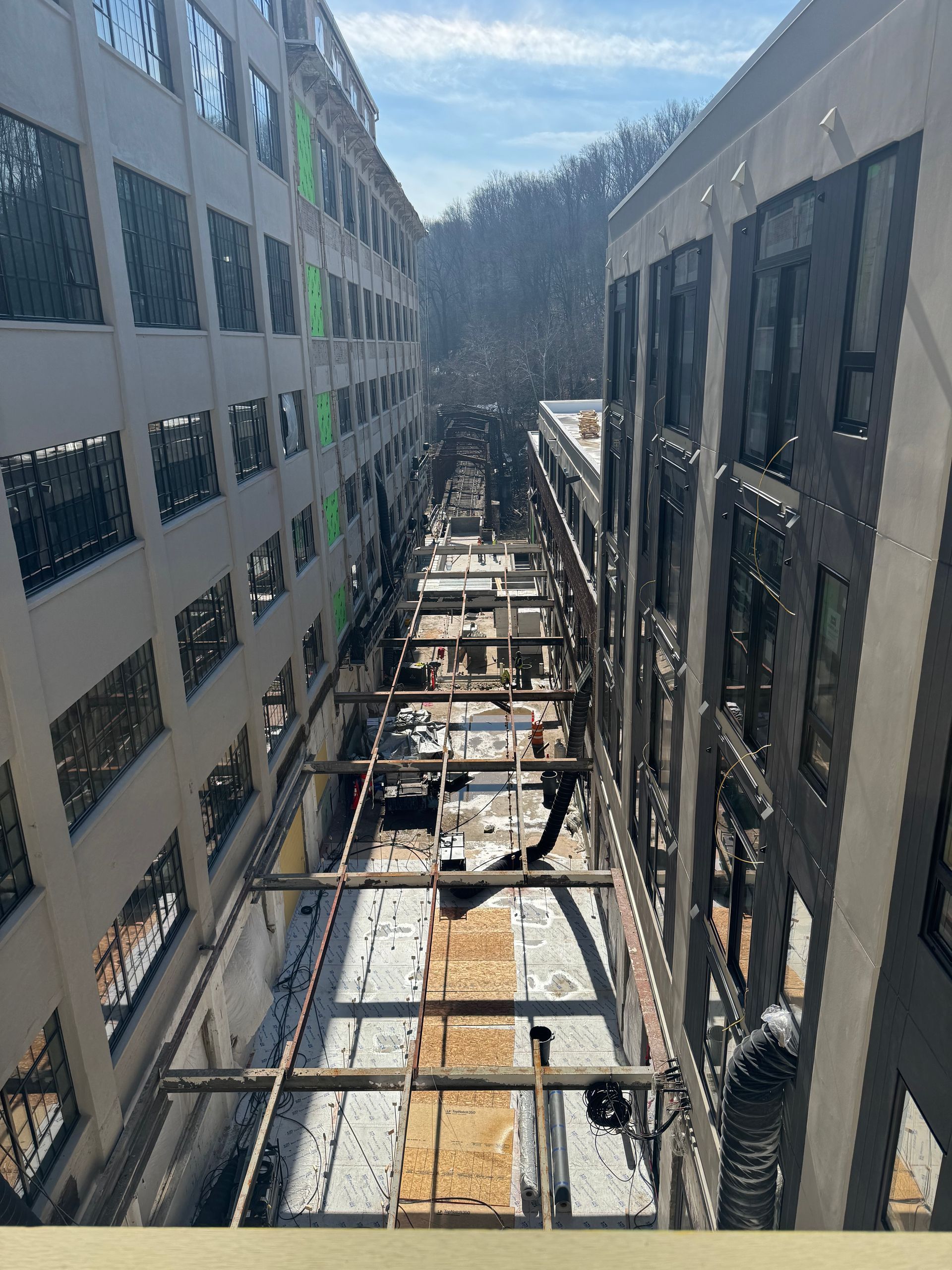 Open-air construction site between two tall buildings with exposed steel framing and snow below