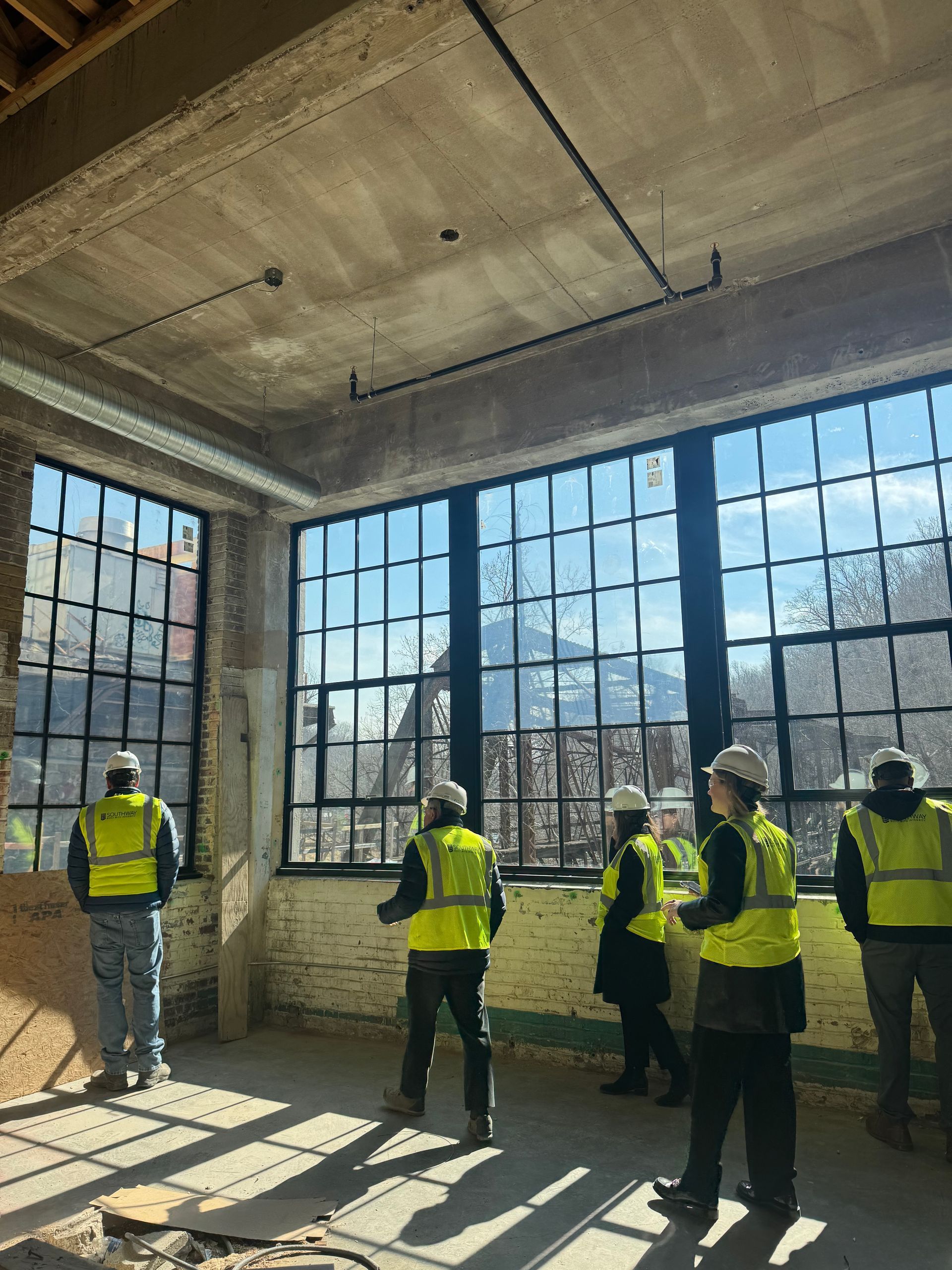 People in yellow safety vests standing in a bright industrial room with large windows