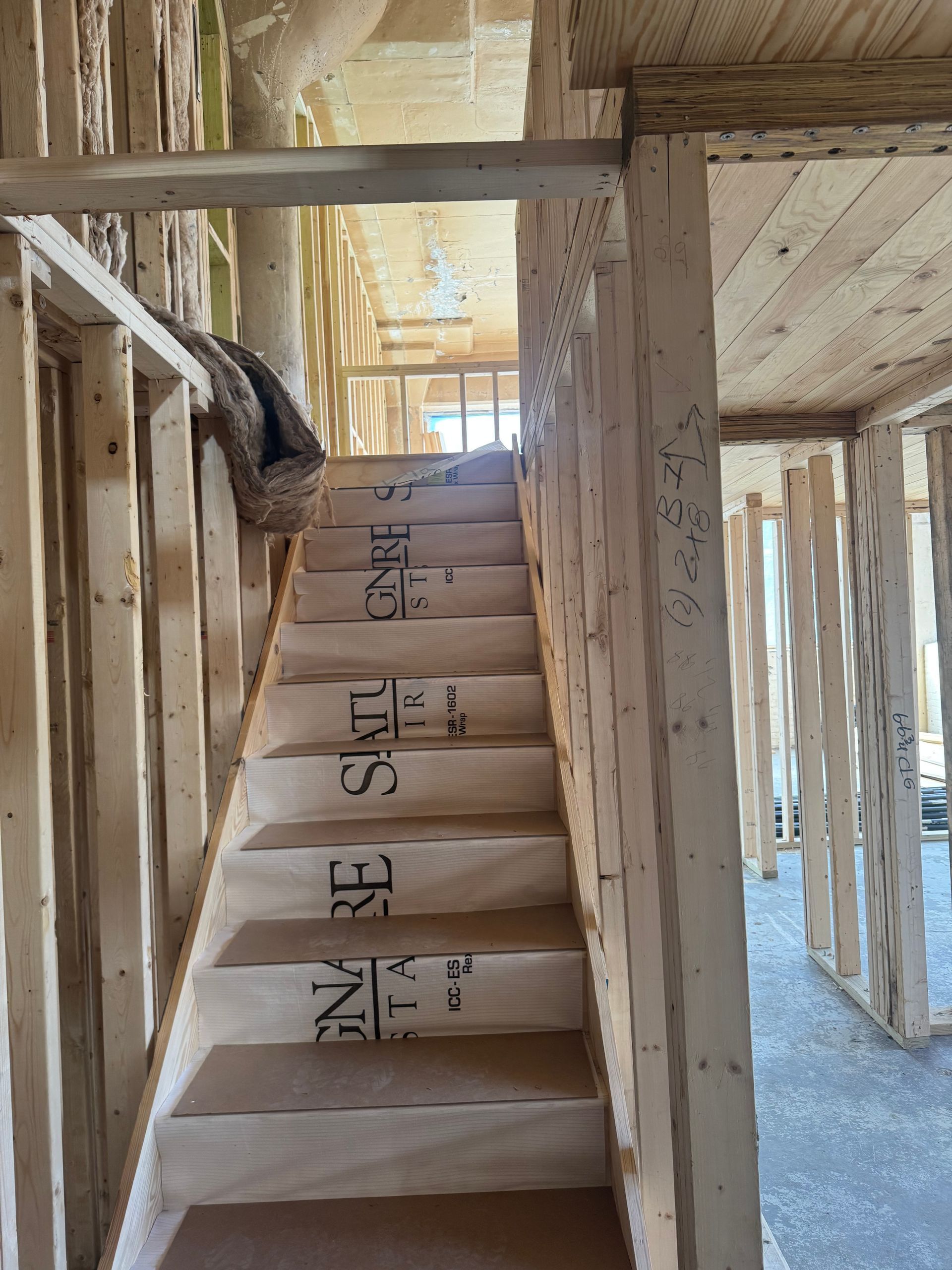 Narrow unfinished wooden staircase in a framed house under construction.