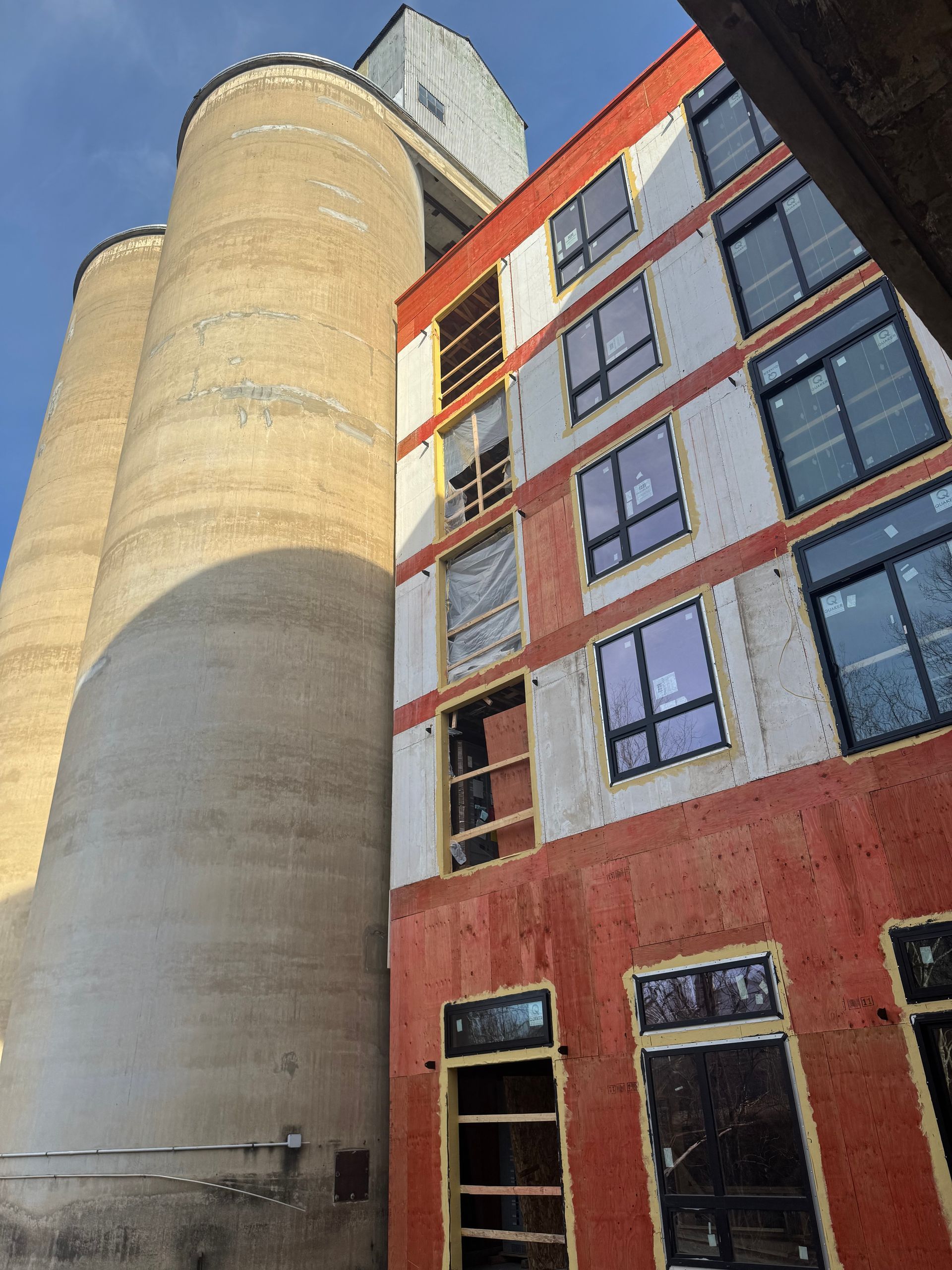 Tall cylindrical concrete tower beside a red brick building with many windows, viewed from below