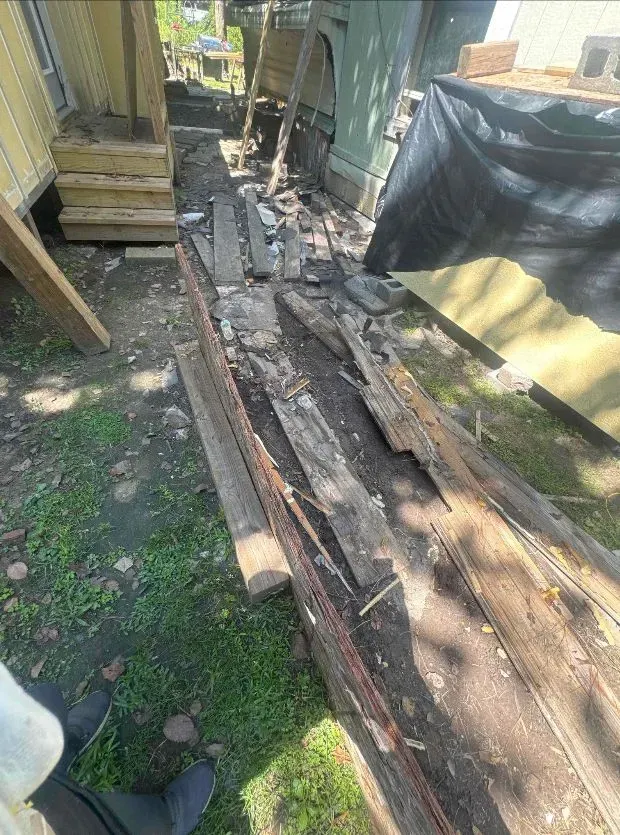 Dilapidated wooden planks on ground between structures; debris.