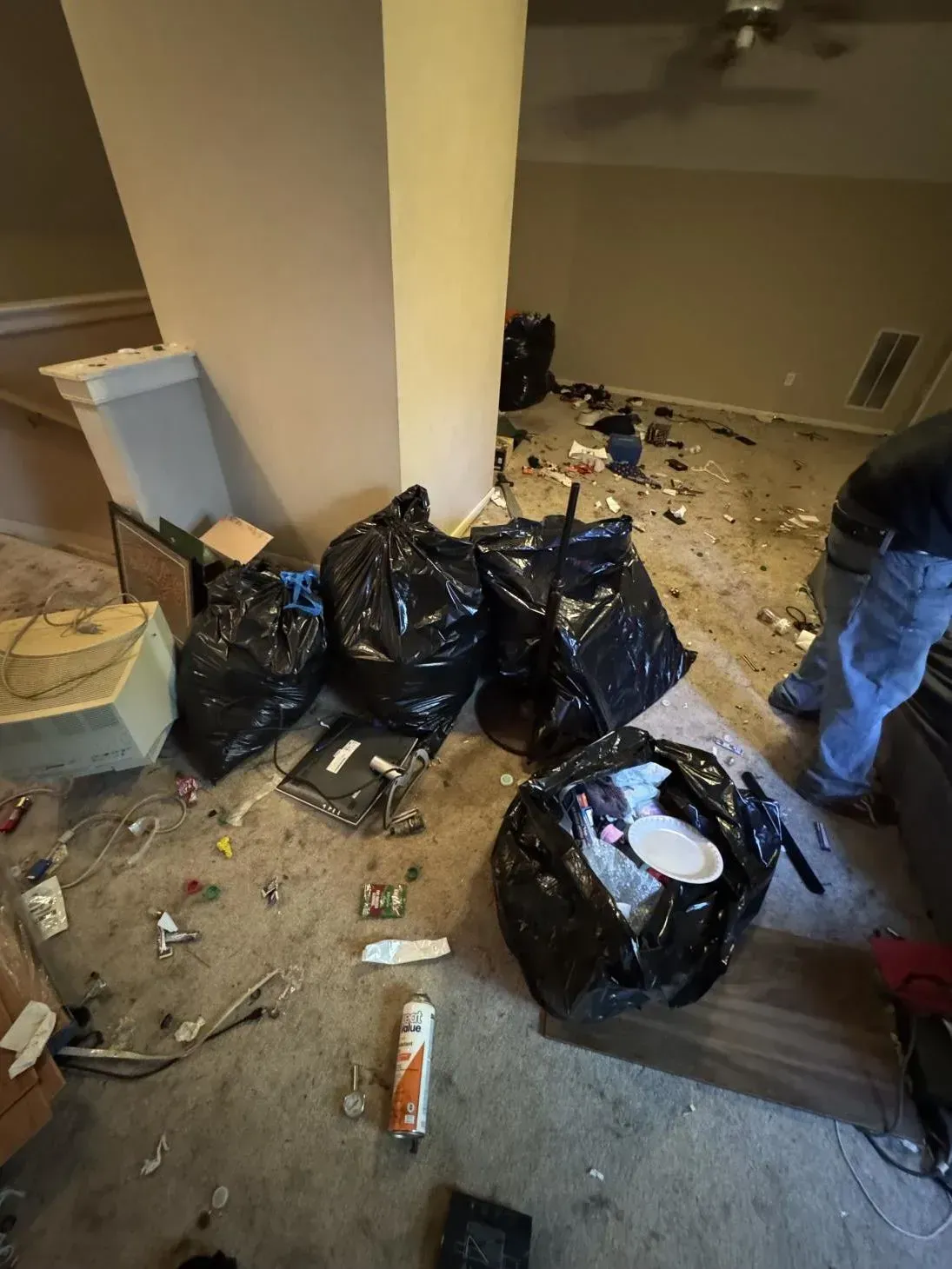 Room with scattered debris, black trash bags, and a person cleaning up.