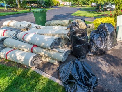 Rags and garbage bags piled on a lawn next to a street. A green bin sits in the background.