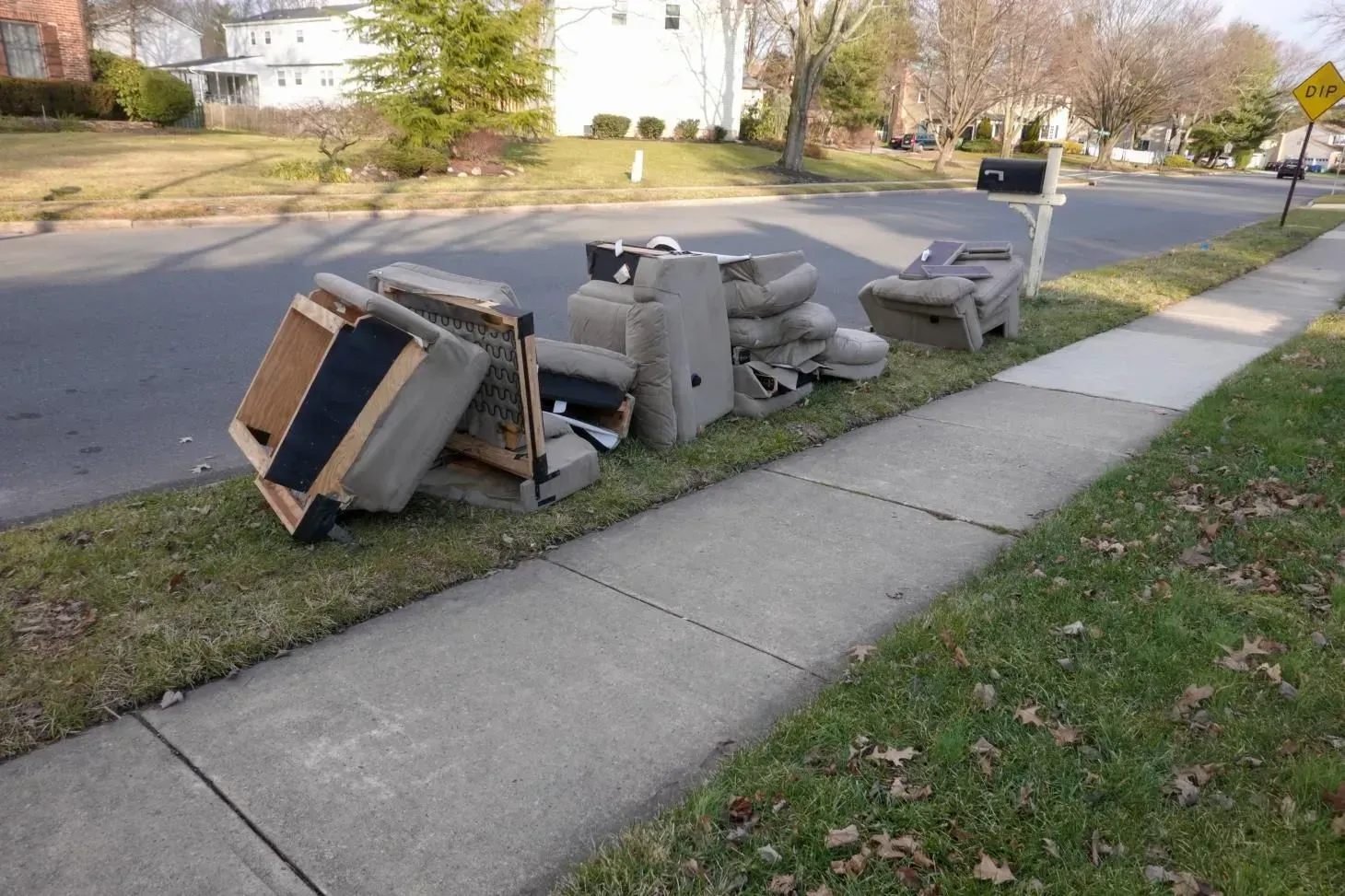Pile of discarded furniture on a residential curb, next to a sidewalk and a mailbox.