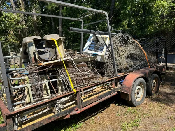 Trailer loaded with scrap metal, including an air conditioning unit and fencing, sitting outdoors.
