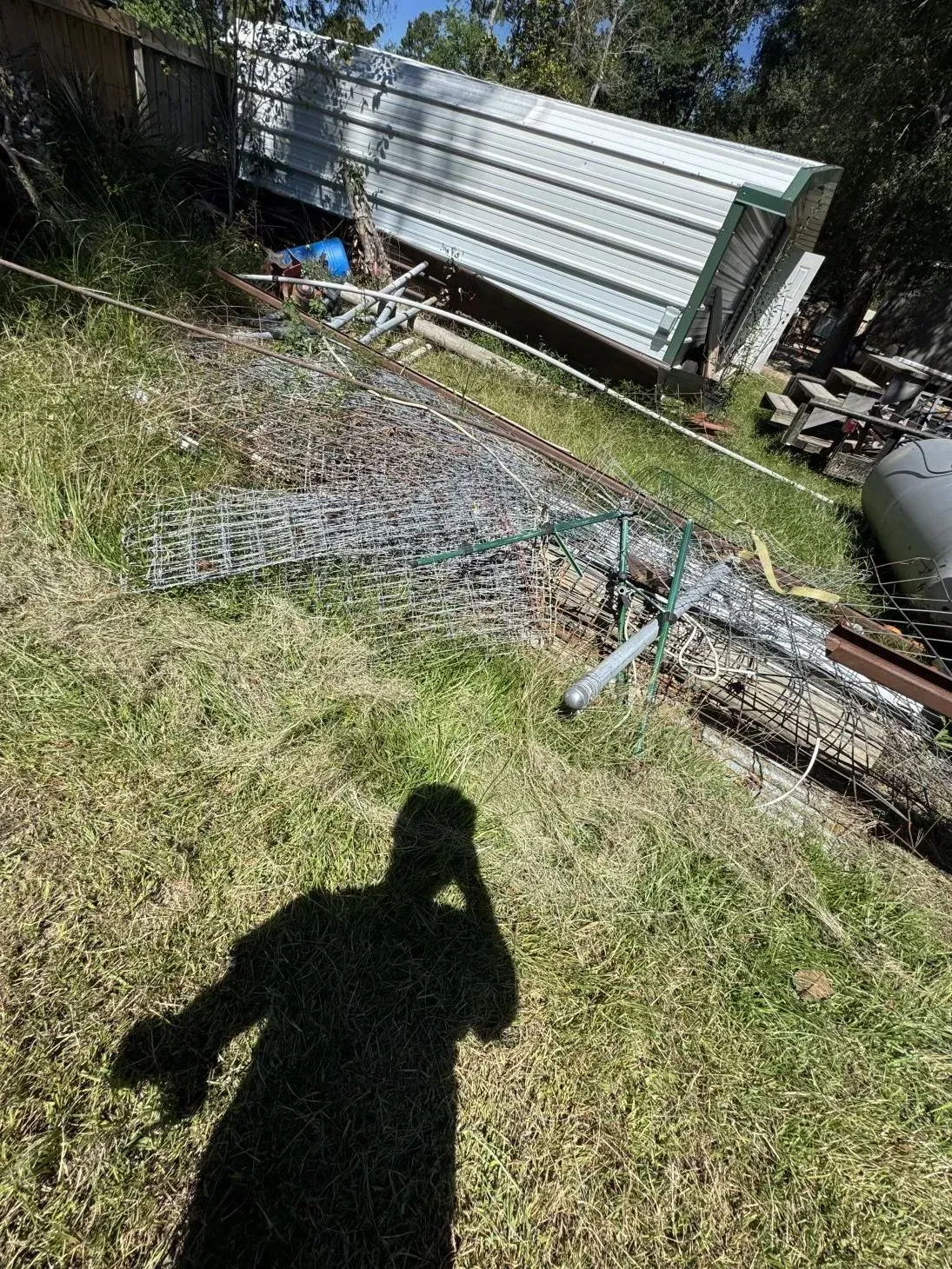 A tilted metal structure on a grassy hillside, debris scattered, a shadow of a person taking the photo.