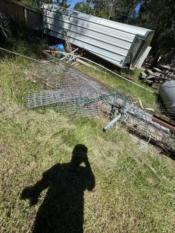A tilted metal structure on a grassy hillside, debris scattered, a shadow of a person taking the photo.