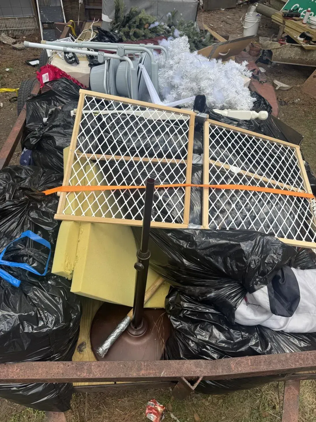 Trailer overflowing with trash bags, baby gate, umbrella base, and other debris.