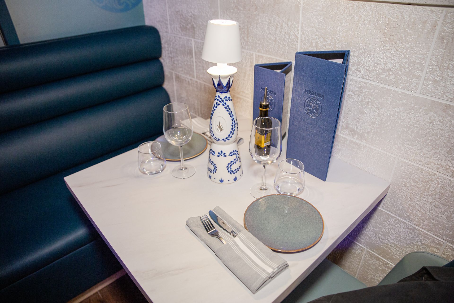 A table in a restaurant with plates , utensils , a lamp and a menu.