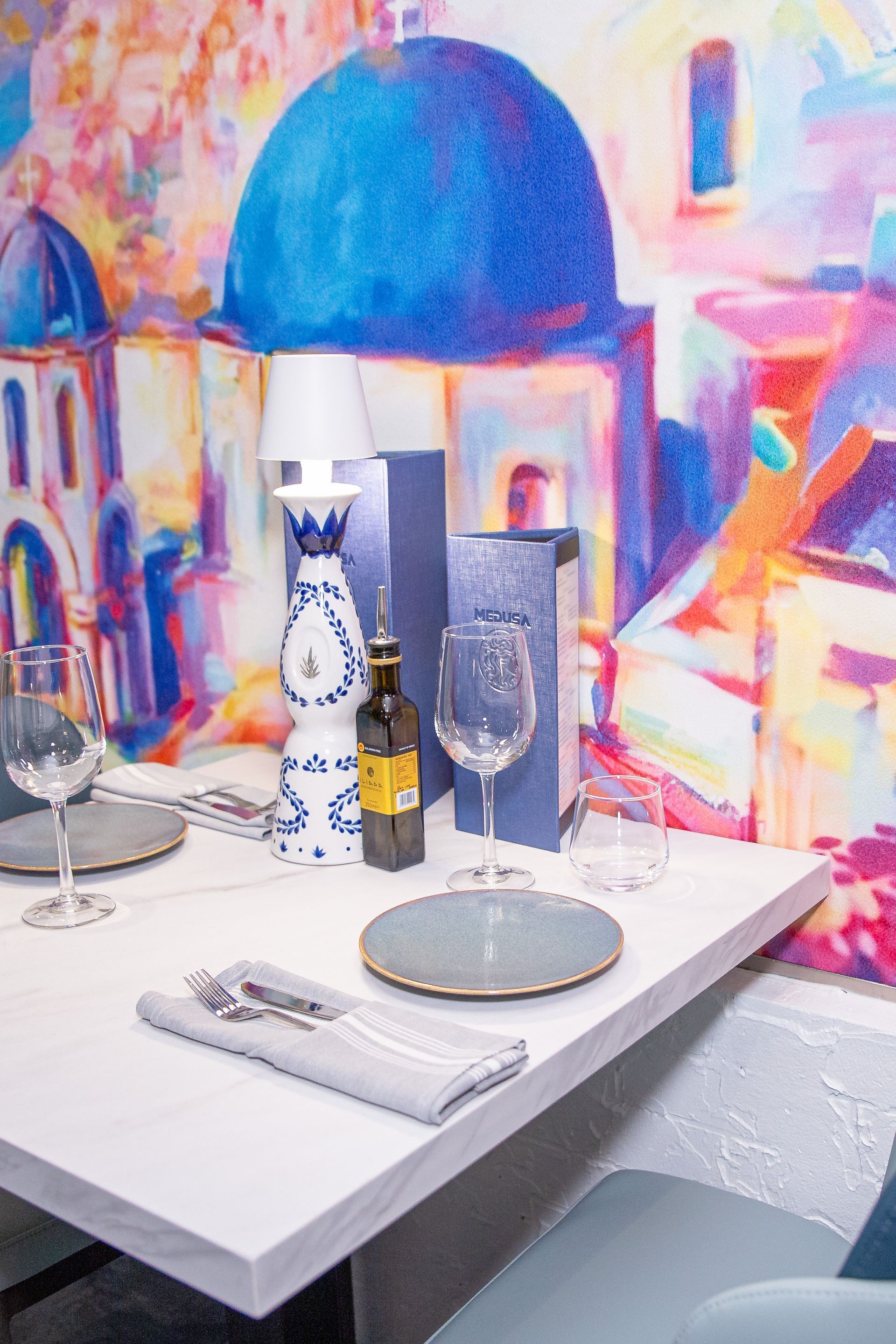 A table with plates , glasses and a bottle of wine in front of a colorful painting.