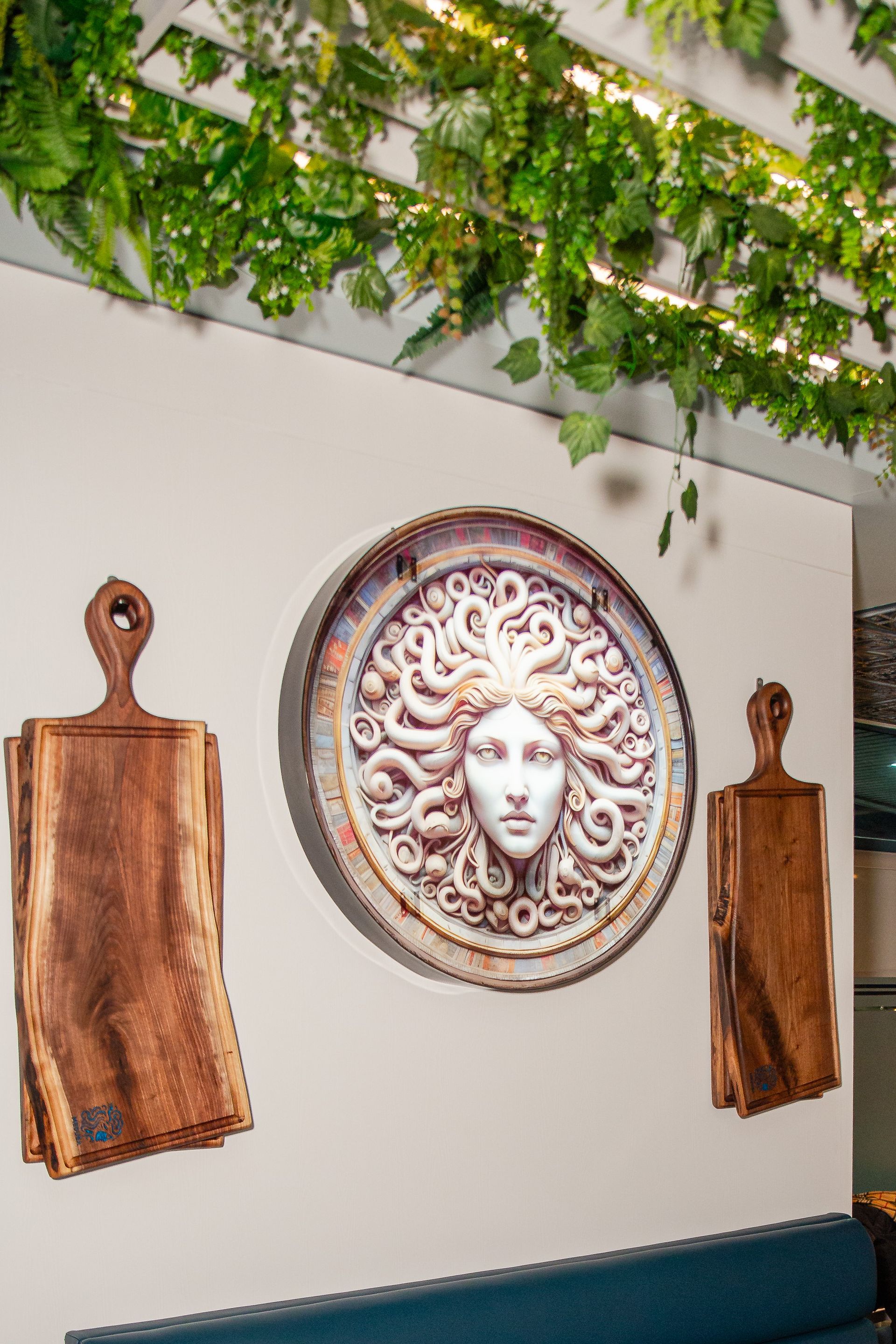 A wooden cutting board with a medusa head on it is hanging on a wall.