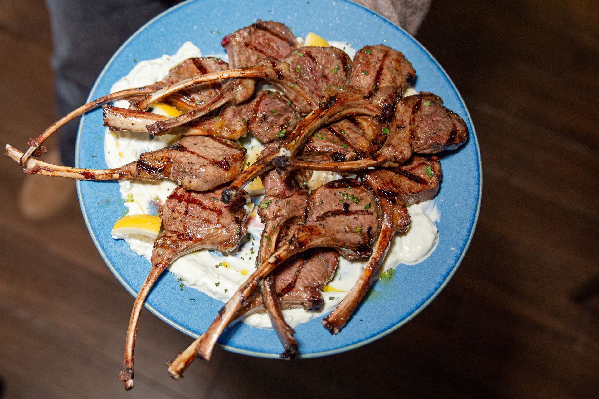 A person is holding a plate of lamb chops on a blue plate.