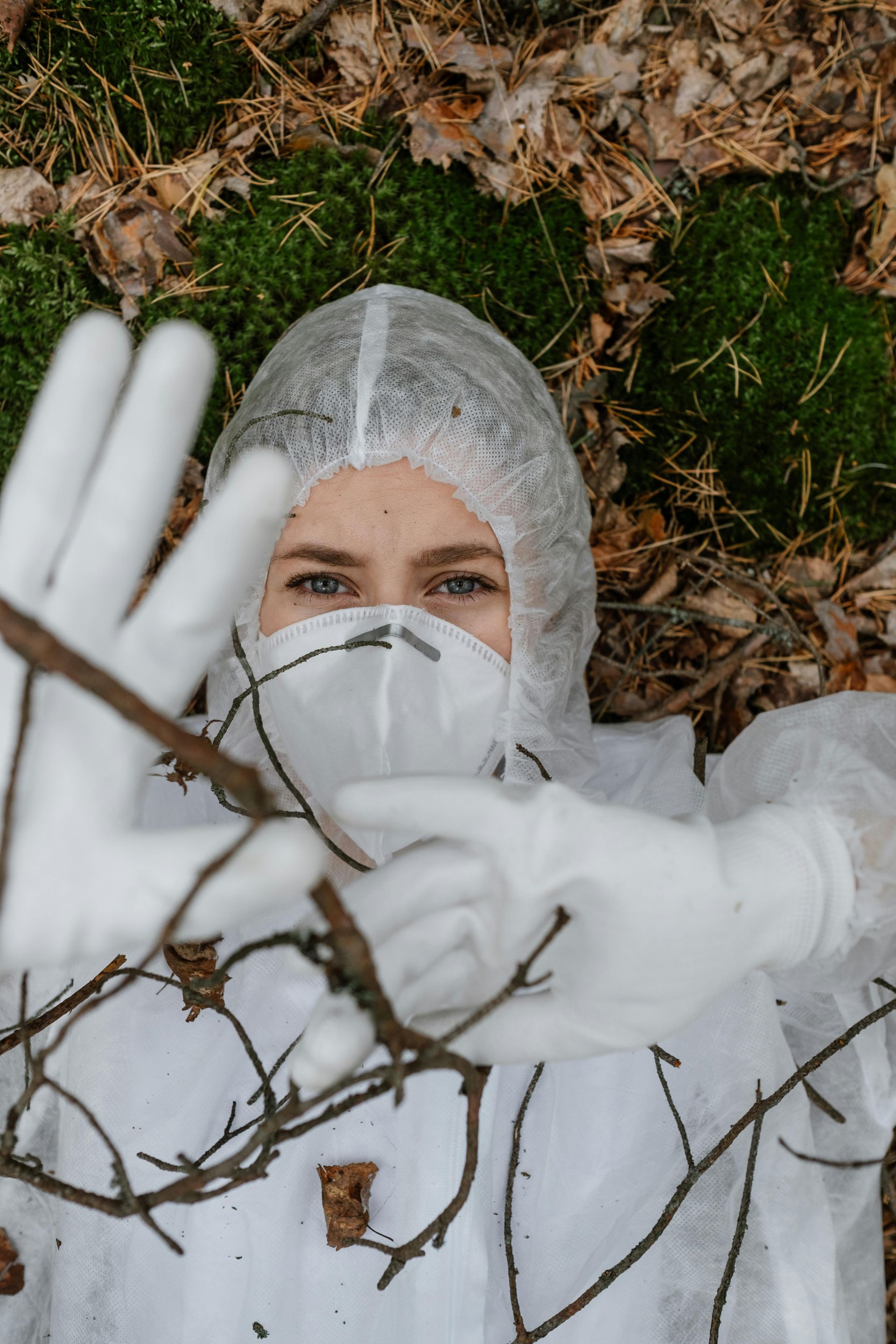 Person wearing blue gloves holding spray bottles, with a yellow cloth and bucket on a surface.