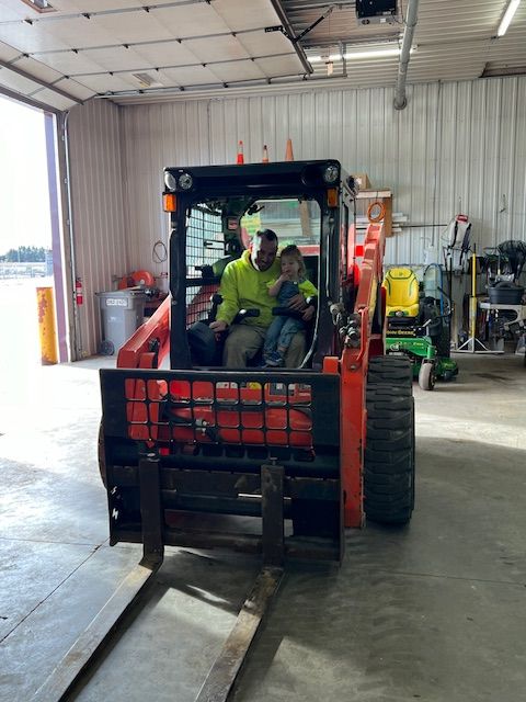 A man and a child are sitting in a tractor in a garage.